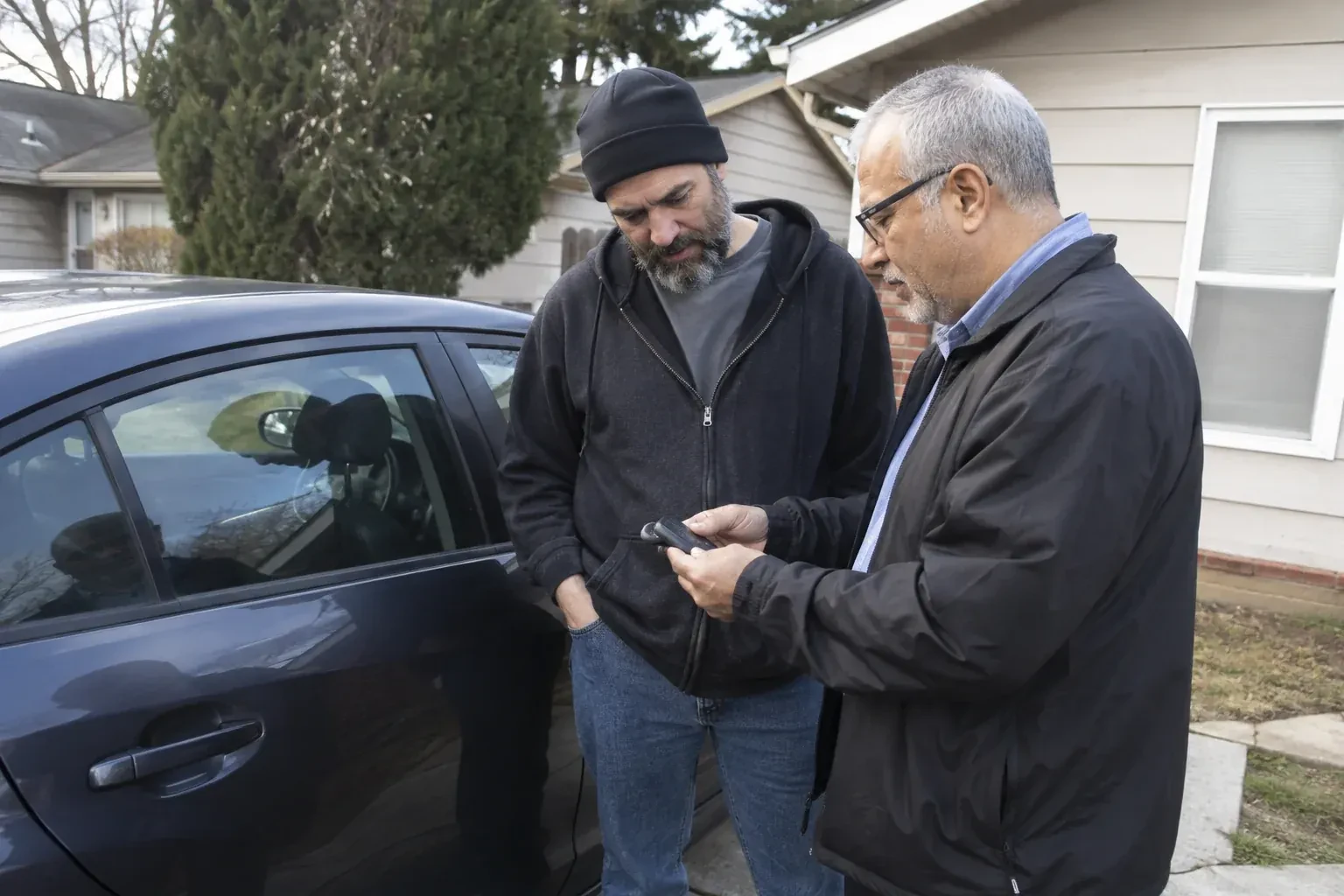 Two adults discussing a key fob beside a parked car. — Car Lockout Service, Niagara Falls