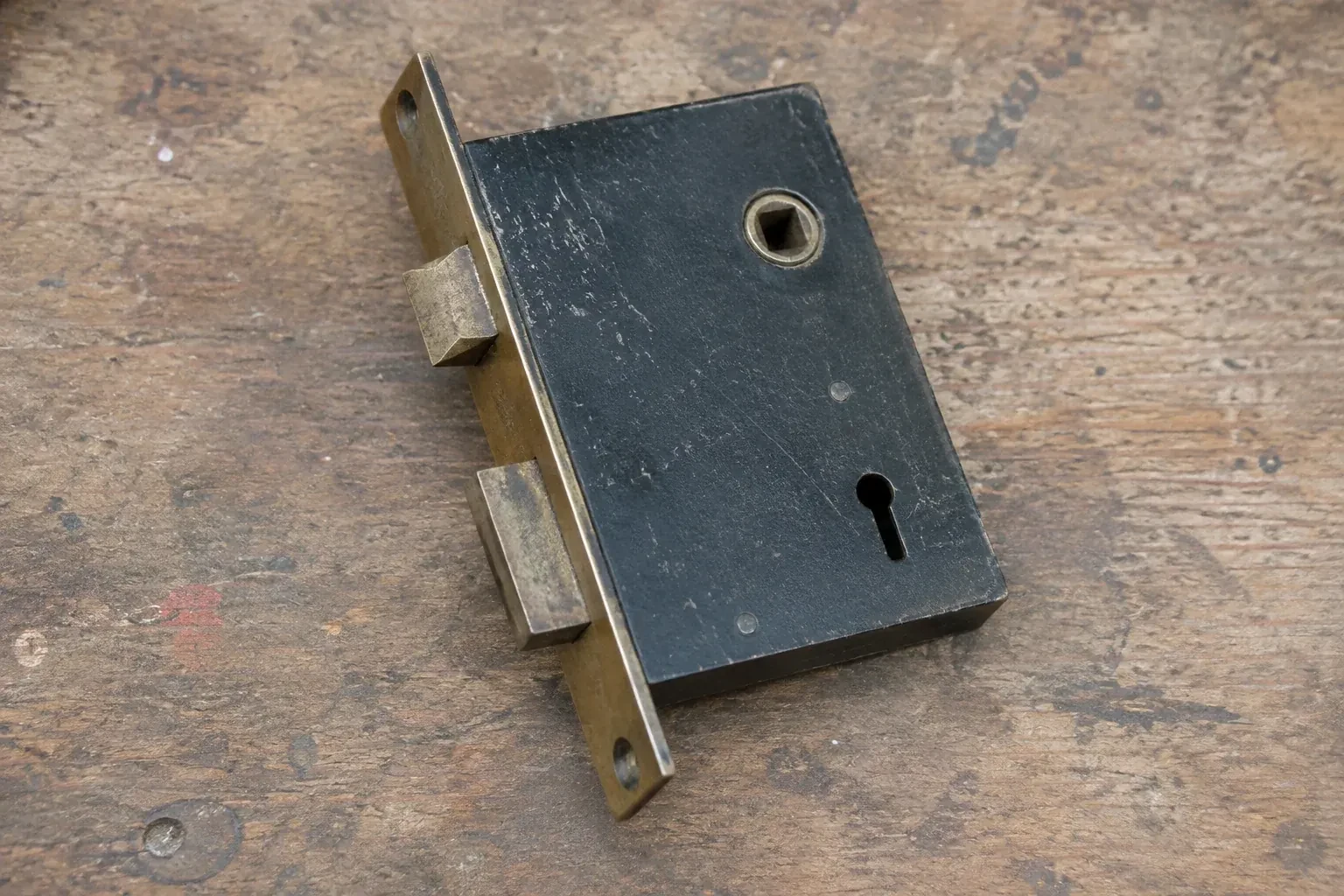 Closed mortise lock case with spindle opening, keyhole, latch and deadbolt on a wooden workbench. — Vintage Mortise Lock Service, Niagara Falls